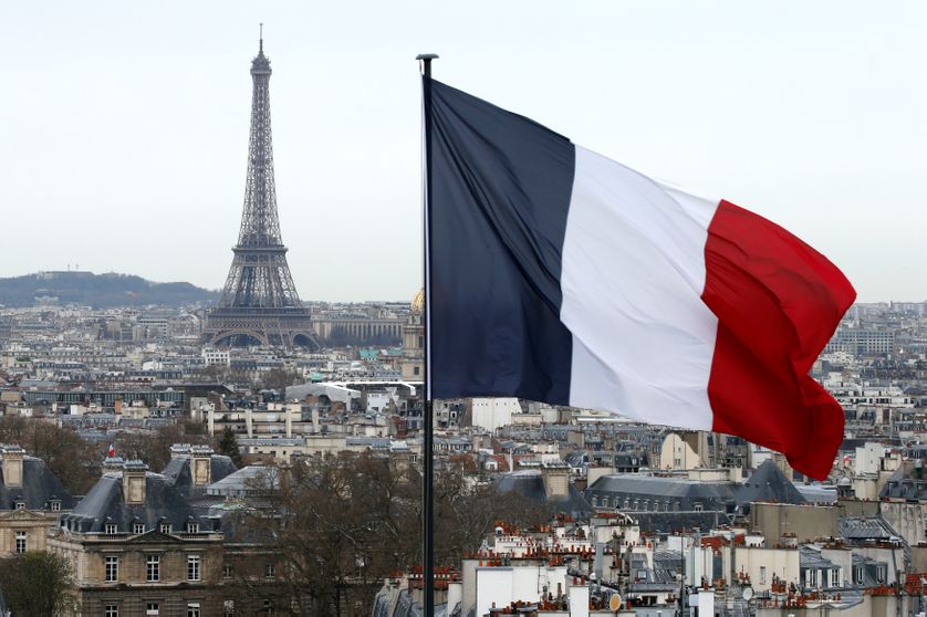 Drapeau français flottant devant les toits de Paris et la tour Eiffel.