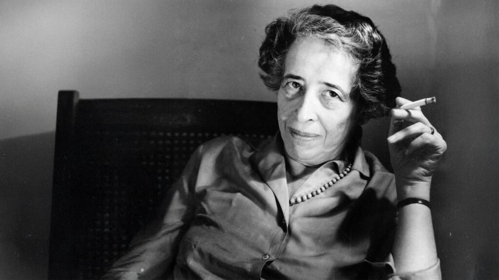 Portrait en noir et blanc de Hannah Arendt tenant une cigarette, philosophe majeure de la pensée politique du XXᵉ siècle.