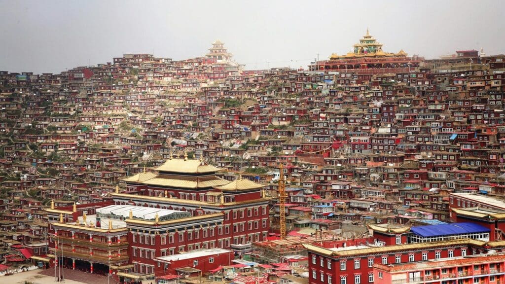 Monastère bouddhiste au Tibet en Chine, entouré de petites maisons rouges traditionnelles dans les montagnes himalayennes.