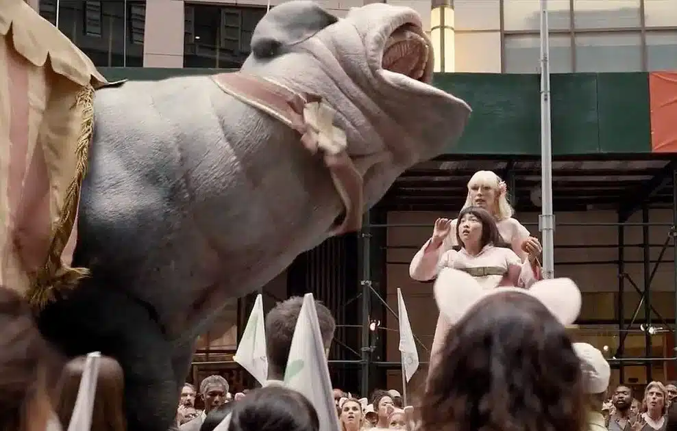 Scène du film Okja – Lucy Mirando (Tilda Swinton) présente le supercochon devant la foule lors d’une cérémonie médiatique, symbole du greenwashing et de la manipulation d’image.