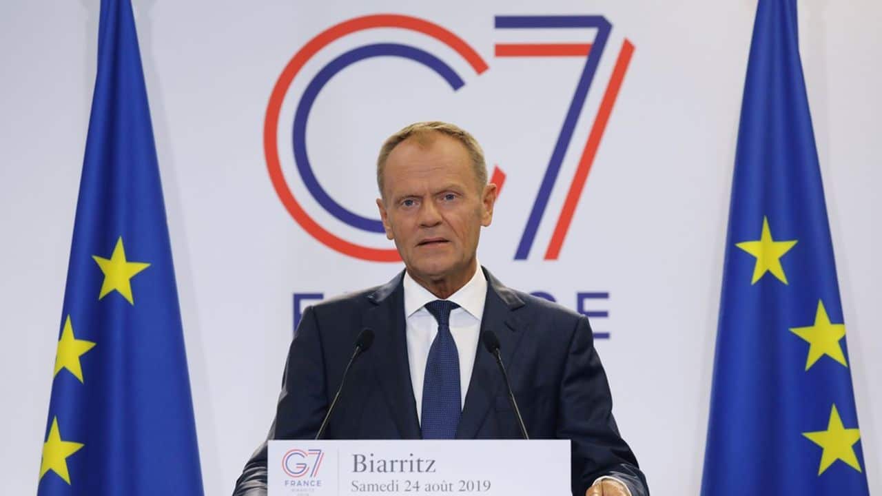 Donald Tusk lors d’un discours avec drapeaux UE, illustrant le retour européen de la Pologne