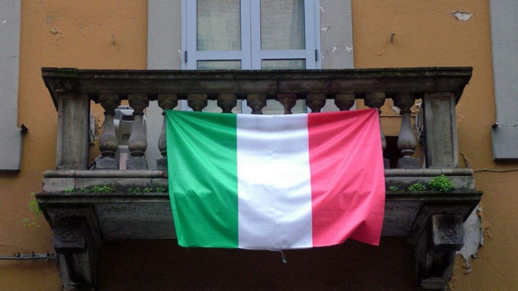 Drapeau italien accroché à un balcon ensoleillé, symbole de l’Italie et de Bella ciao