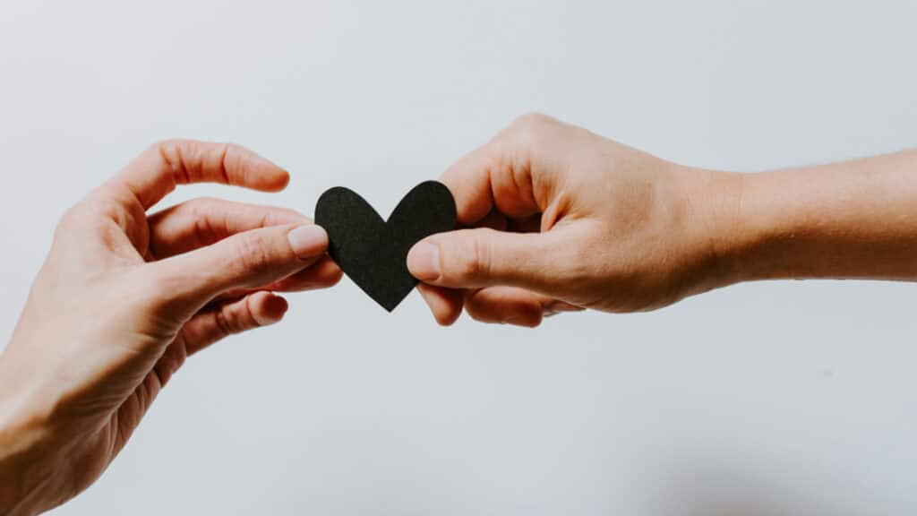 Deux mains s'échangeant un cœur en papier noir, illustration poétique de l'amour et du dire amour en littérature