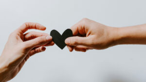 Deux mains s'échangeant un cœur en papier noir, illustration poétique de l'amour et du dire amour en littérature