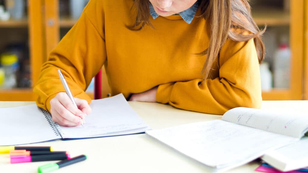 Étudiante rédigeant un essay en anglais sur un cahier, surlignée de stylos colorés