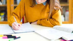 Étudiante rédigeant un essay en anglais sur un cahier, surlignée de stylos colorés