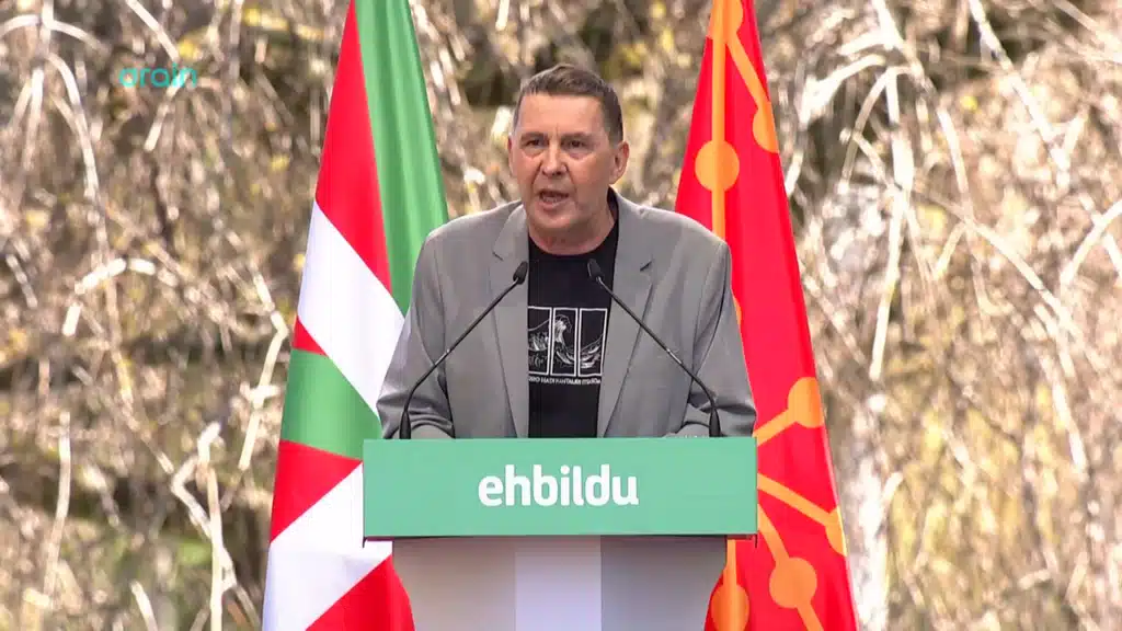 Arnaldo Otegi prenant la parole derrière un pupitre EH Bildu, entouré des drapeaux basque et navarrais