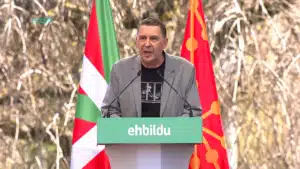 Arnaldo Otegi prenant la parole derrière un pupitre EH Bildu, entouré des drapeaux basque et navarrais