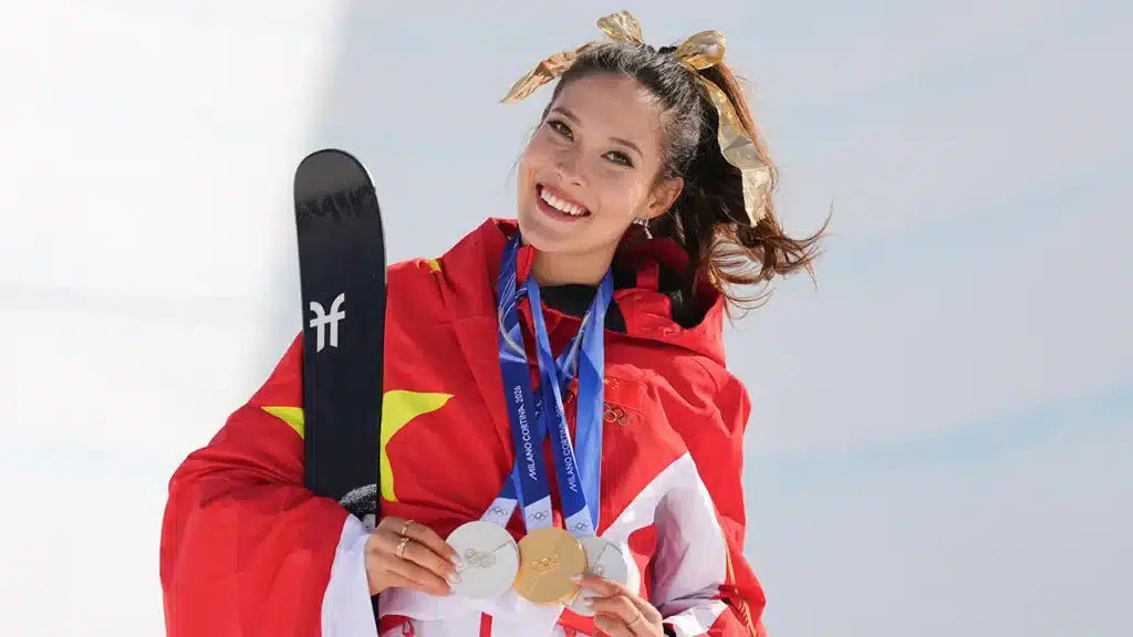 Eileen Gu souriante avec ses médailles olympiques, enveloppée du drapeau chinois