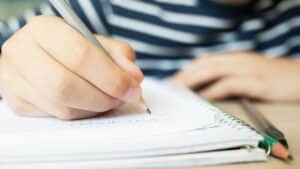 Main d'étudiant écrivant dans un cahier ligné pour analyser les figures de style d'un texte littéraire