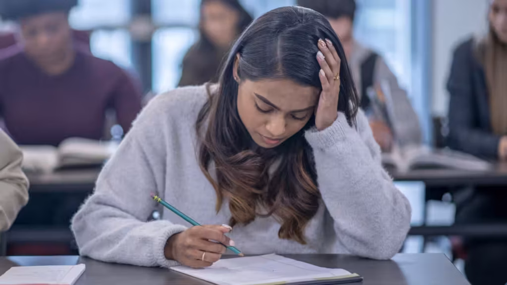 Étudiante concentrée pendant un examen, le front appuyé sur sa main, illustrant la difficulté du prétérit modal en anglais