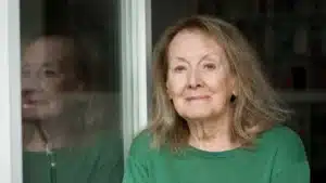 Portrait d'Annie Ernaux en pull vert devant une vitre, auteure dont le style littéraire est au programme de khâgne
