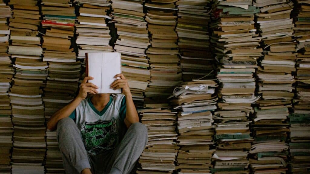 Étudiant entouré de piles de livres révisant les sujets oral anglais