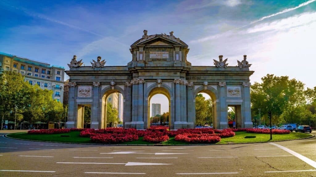 La Puerta de Alcalá à Madrid entourée de fleurs rouges, illustration pour apprendre devenir en espagnol