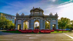 La Puerta de Alcalá à Madrid entourée de fleurs rouges, illustration pour apprendre devenir en espagnol