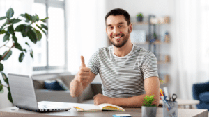 Jeune homme souriant devant un cahier et un ordinateur, illustrant le travail comme réalisation de soi